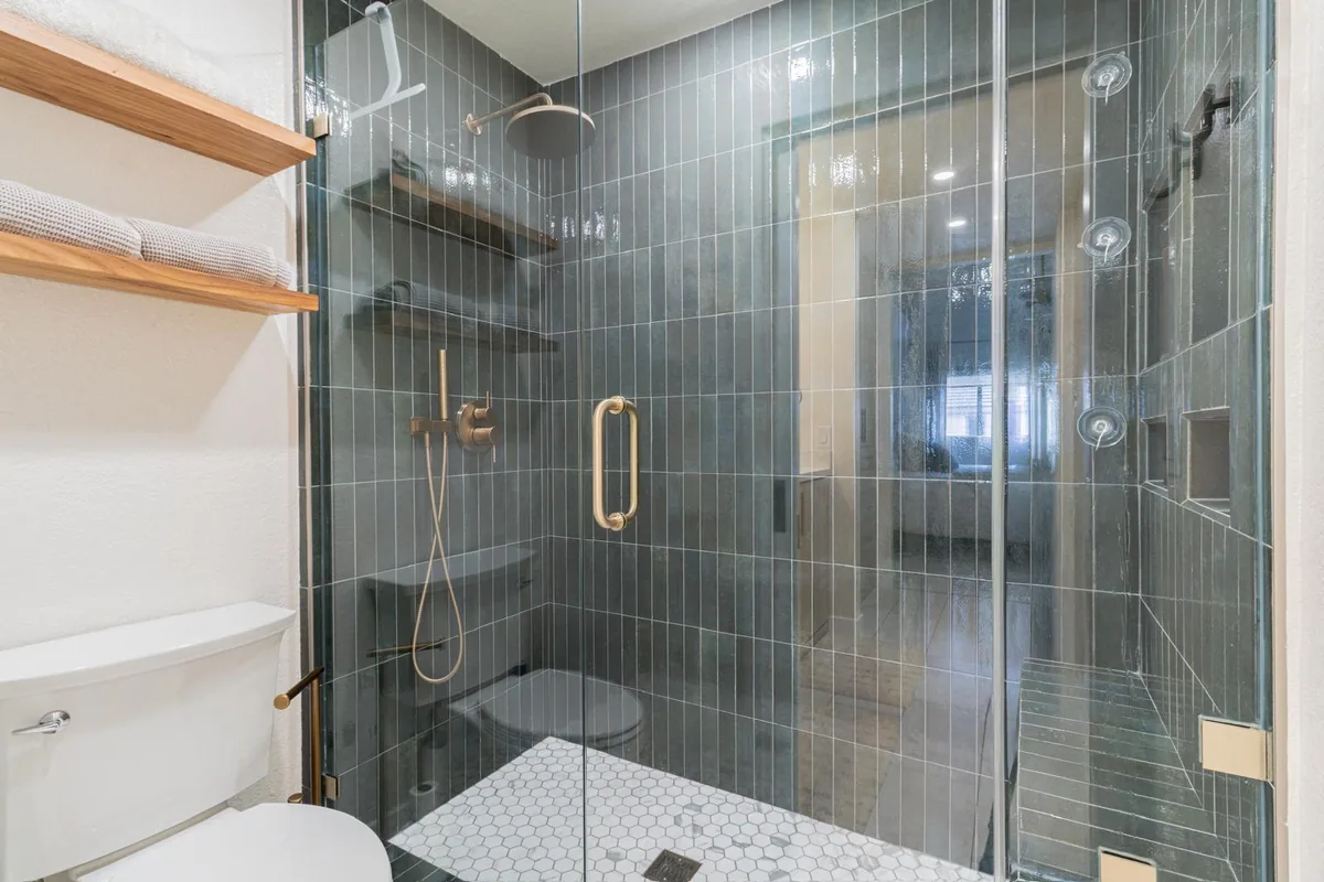 Teal vertical tile walk-in shower with brass fixtures and oak shelving